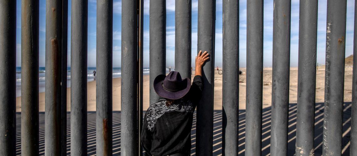 A man looks towards the United States through a fence in Tijuana, Mexico.
